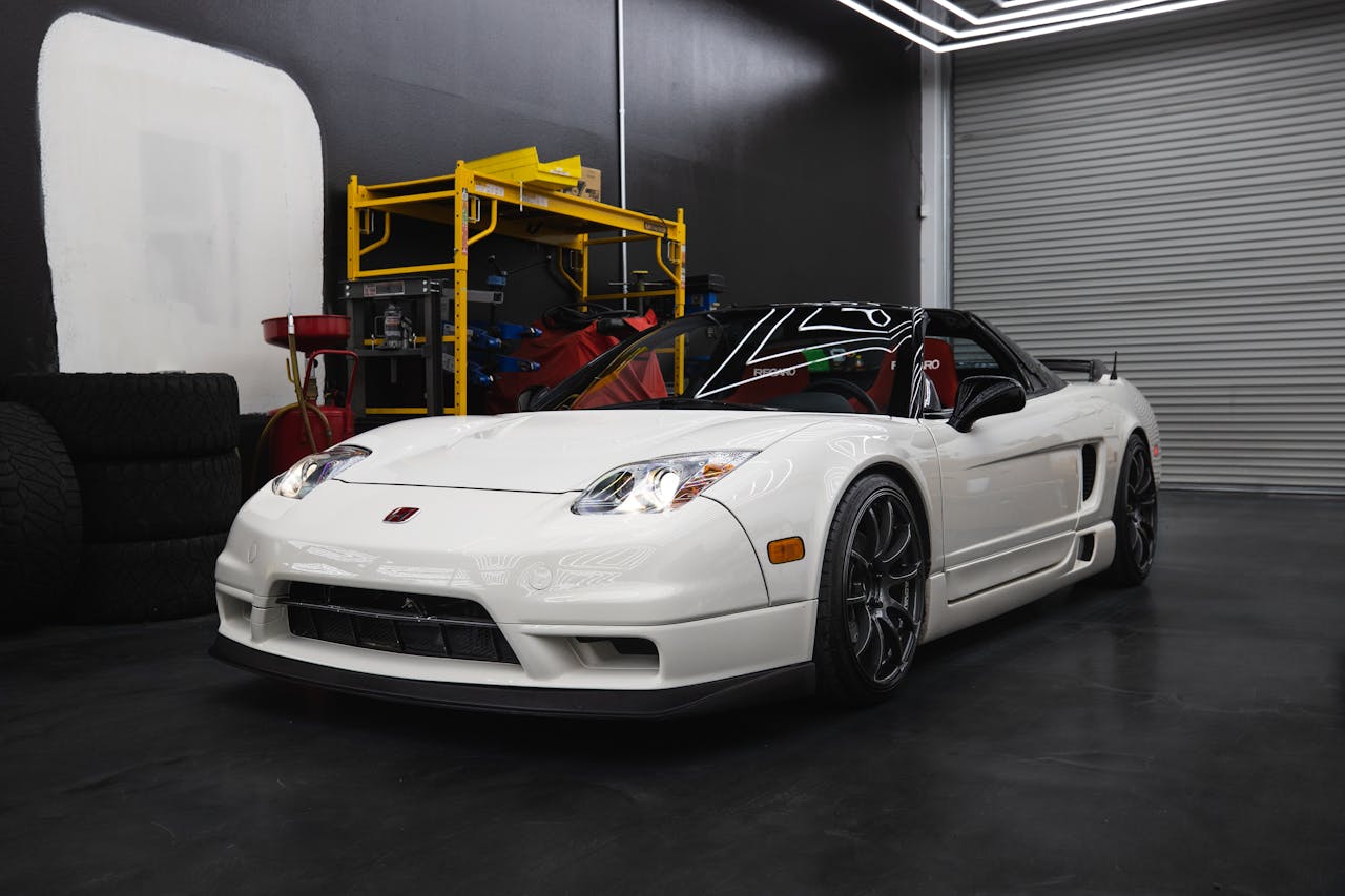 A luxurious white sports car parked in a contemporary garage with industrial equipment.