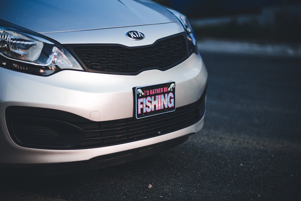 Front view close-up of a Kia Rio car featuring a humorous fishing-themed license plate frame.